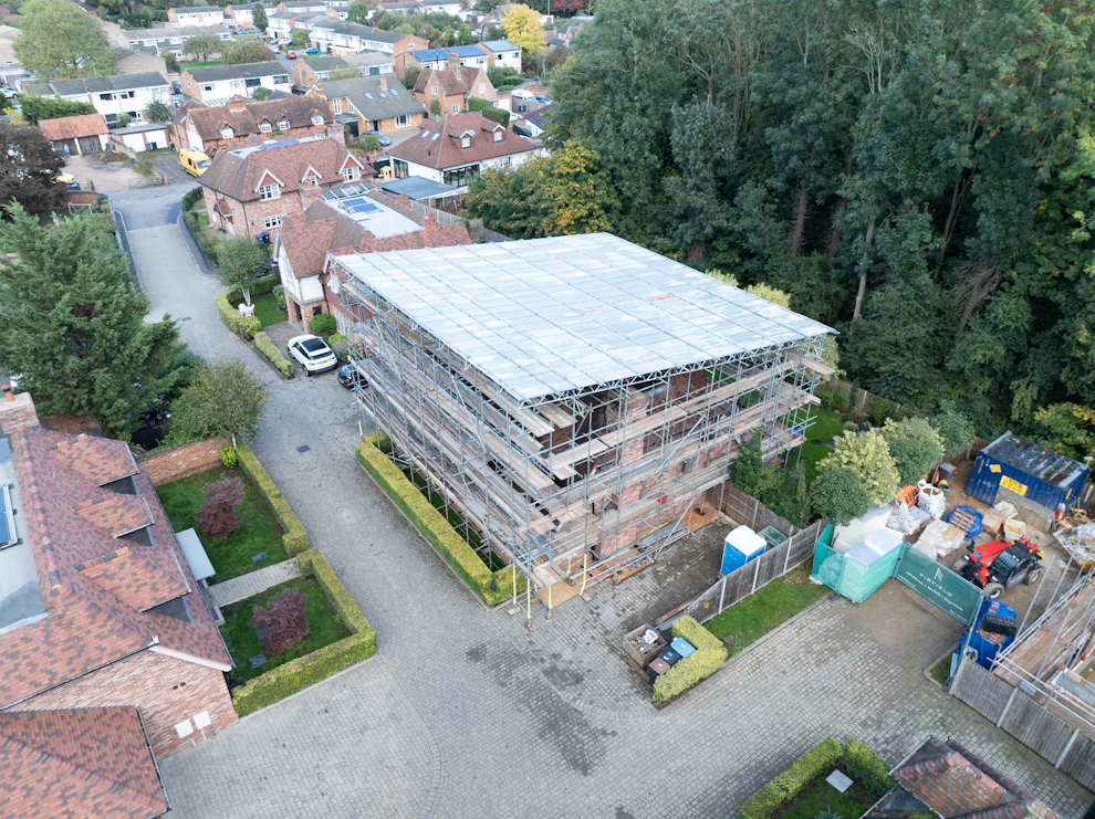 Drone image showing a scaffolded house surrounded by residential buildings and trees