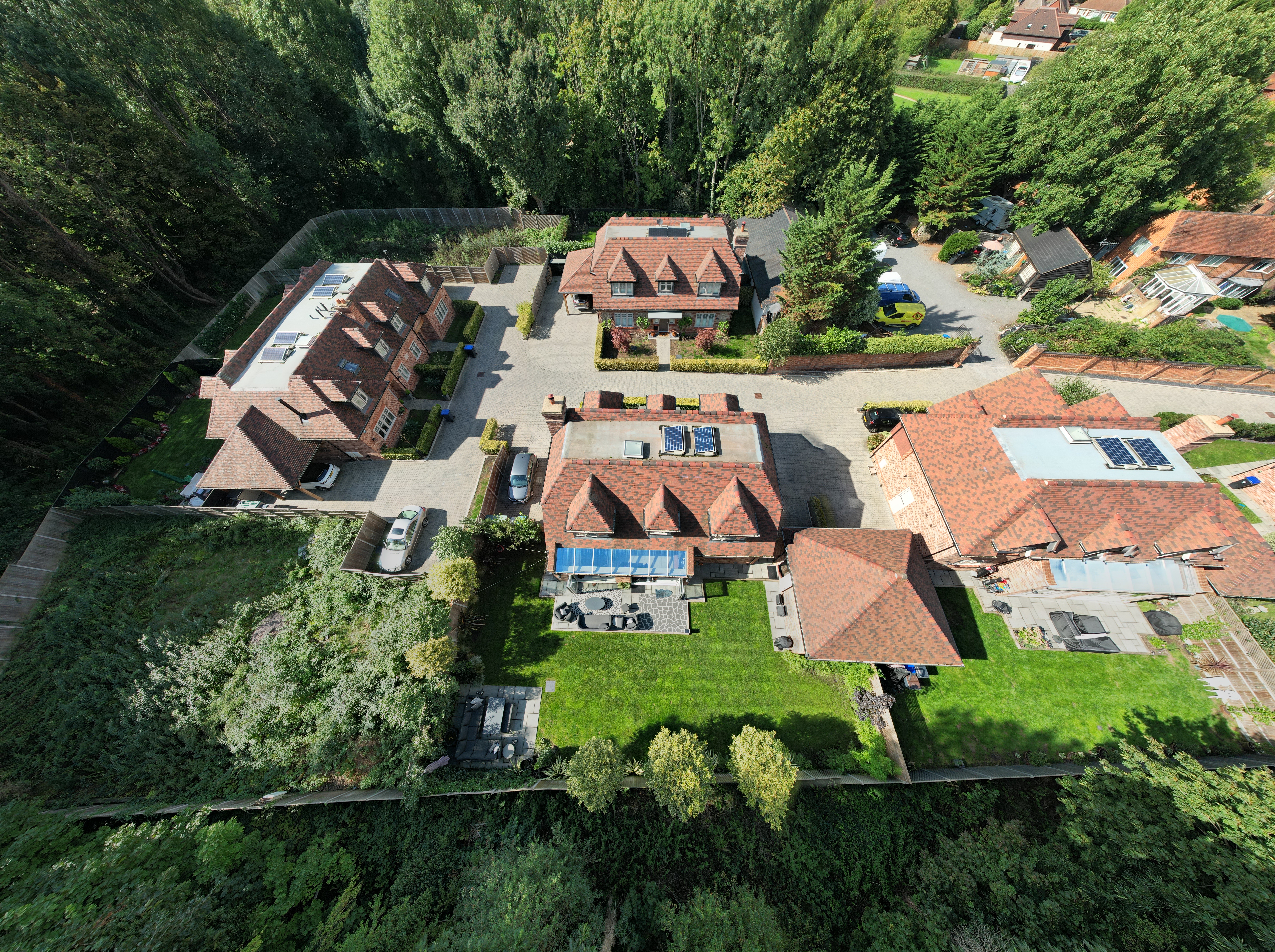 High-angle aerial photo of a large residential property with multiple buildings, gardens and surrounding trees.